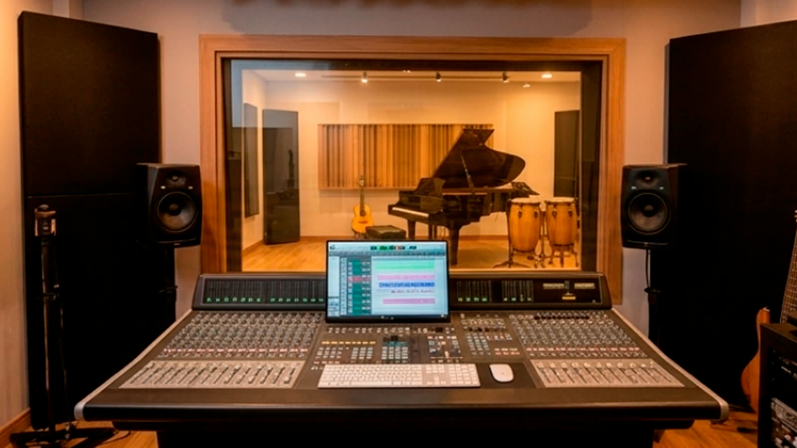 Estúdio de gravação do IMTW com mesa de mixagem e, ao fundo, sala com piano de cauda, violão e percussão.